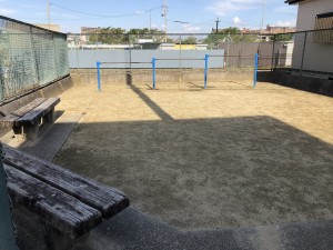 土の地面の広い敷地に、ベンチと鉄棒が設置されている公園の写真