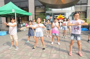 屋外で子どもたちが自分の胸の前で手と手を合わせてダンスを練習している様子の写真