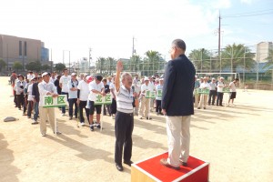 忠岡町民ゲートボール大会の開会式で参加者が整然と並び、朝礼台に立った主催者の前で参加者代表が右手を挙げて選手宣誓をしている様子を撮影した写真