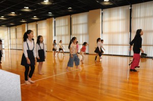 キッズクラブの時間に室内練習場で先生のお手本を見ながらダンスの練習をする子供たちの写真