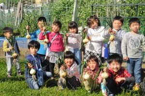 玉ねぎ畑で収穫したばかりの玉ねぎを手に持ちカメラに向けている子どもたちの集合写真