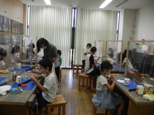 夏休み紙粘土教室で先生に教えられながら真剣に自分の作品作りに取り組む子供たちを教室の正面から撮影した写真