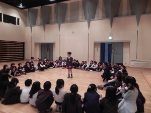 お楽しみ会で円形に並んで座っている学生と、その円の中心に立つ男の子の写真