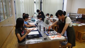 「かき方習字」の教室で朱墨で書かれたお手本を参考に、子どもたちが習字を練習している写真