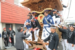 法被や浴衣姿でだんじりに乗った人たちにうちわを渡す写真