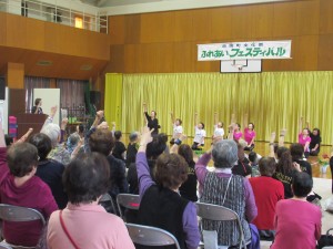 忠岡町文化祭ふれあいフェスティバルで観客と一緒になって右腕を上げてフェスティバルを盛り上げるいこい会のメンバーの写真