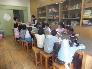 毛糸を使った手編み教室の様子と先生の説明を興味深そうに聞く子どもたちの写真