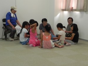 福祉センターの一室の片隅で、子どもたちがご年配の方たちと集まって何かのゲームを床でしている様子の写真