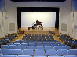 ステージ上にピアノが設置され、その調律をしている人を客席後方から撮影した写真