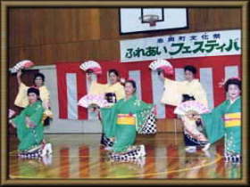 紅白幕の前で扇子を持ち踊っている女性たちの写真